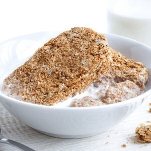 White bowl with two whole wheat breakfast biscuits isolated on white with milk, bottle and spoon. Crumbs on placemat and partly eaten.