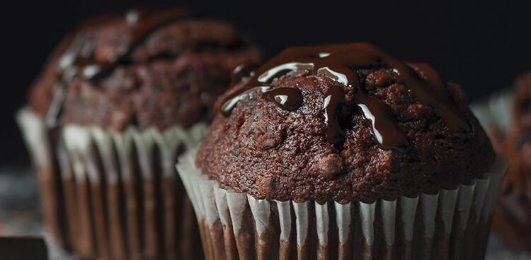 Close up of cocoa muffins with chocolate icing on rustic table covered with sugar and cocoa with vintage spoon and blank space