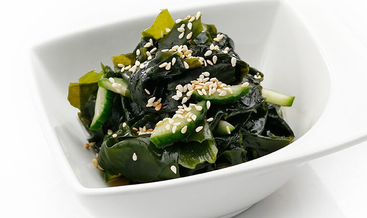 Cucumber and wakame seaweed salad with a sesame seeds, isolated on a white background. Sunomono in a white elegant bowl. Japanese delicacy, sushi restaurant menu.