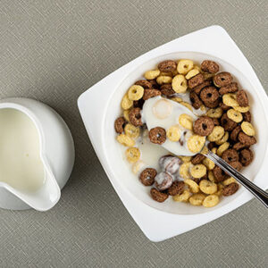 Pitcher with yogurt, spoon in white bowl with toasted cereal breakfasts and yogurt on gray table. Top view