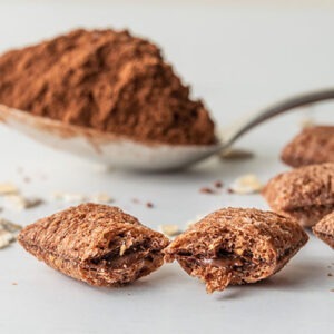 Delicious filled chocolate or cocoa pillows in a macro view, for breakfast or snack. On a white background with several oatmeal flakes and a spoon with cocoa powder.