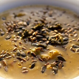 Creamy vegetables soup with rousted sunflower and pumpkin seeds and pesto in white plate. Healthy food.